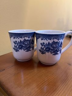 two blue and white cups sitting on top of a wooden table