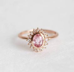 Oval peach-pink sapphire & diamond halo ring in 14k or 18k gold, depicted in rose gold. Perfect as an engagement or wedding ring. ★Details Main gemstone: peach-pink sapphire Shape: oval Weight: approx. 0.75-0.77 ct Quality: VS-VVS clarity grade Treatment: none Halo stones: white diamonds (16) Shape: round Measureme Peach Sapphire Rings, Pink Sapphire Diamond Ring, Pink Sapphire Ring Engagement, Gold Sapphire Ring, Peach Sapphire, Diamonds Rings, Flower Engagement Ring, Sapphire Rings, Diamond Halo Ring