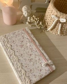 a white book with lace and flowers on it next to a basket, candle and vase