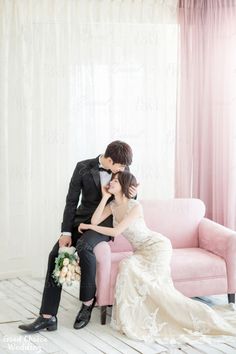 a bride and groom sitting on a pink couch in front of a white drapes