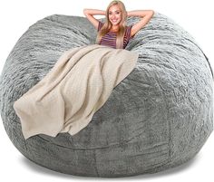 a woman sitting on a large bean bag chair with her arms behind her head, wrapped in a blanket