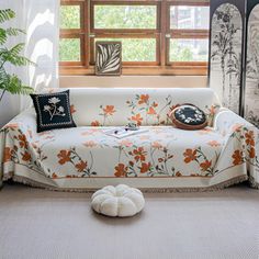 a living room with a white couch and orange flowers on the cover, next to a window