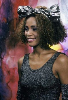 a woman with curly hair wearing a silver dress and a big bow on her head