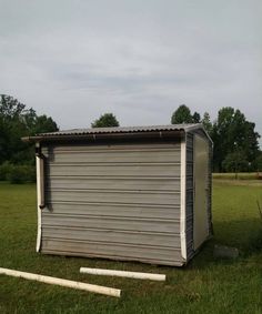 an outhouse sits in the middle of a field with baseball bats laying around it