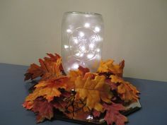 a glass jar filled with autumn leaves on top of a table