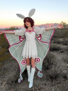 a woman dressed in an angel costume standing on top of a dirt field with her arms outstretched