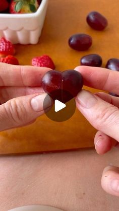 a person holding a piece of fruit in their hand with berries on the table behind them