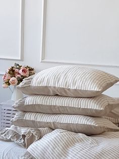 a stack of pillows sitting on top of a bed next to a vase with flowers