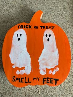 an orange painted pumpkin with two white ghost faces and words trick or treat smell my feet