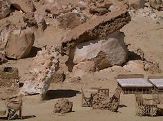 several chairs and tables in the desert near large rocks, including one that has been carved into it