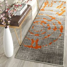 an orange and gray area rug in a living room next to a vase with flowers