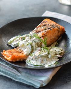 a black plate topped with salmon and coleslaw next to a glass of water