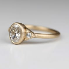 a yellow gold engagement ring with an oval diamond in the center and two small diamonds on each side