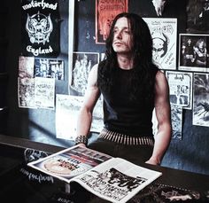 a man with long hair sitting at a table in front of a magazine and looking up