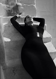 a woman laying on top of a stone wall next to a white brick wall with her hands behind her head