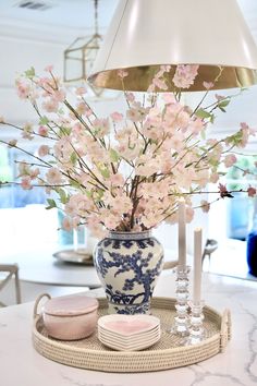 a blue and white vase filled with pink flowers on top of a tray next to a lamp