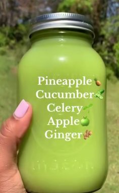 a person holding a green jar with the words pineapple cucumber celery apple ginger on it