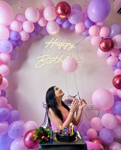 a woman sitting at a table in front of a balloon arch with the words happy birthday on it