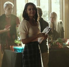 a woman standing in front of a group of people holding papers and talking to each other