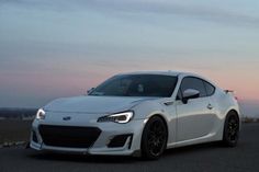 a white sports car is parked on the side of the road at sunset or dawn