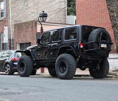 a black jeep parked on the side of a road next to a tree and brick building