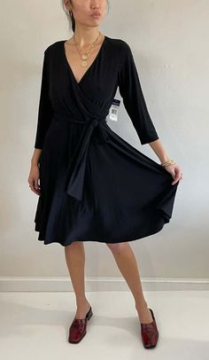 Vintage deadstock ralph lauren faux wrap dress featuring surplice neckline matching sash and swing skirt.  lightweight stretchy black knit - a minimalist treasure.    bust 42-49 waist 34-39 hips 78-80 length 42  bodice length 17.5   shoulder 16 sleeve 18    y2k chaps ralph lauren 95% poly 5% spandex tag size xl new with tags.    model is 5'10 size 2/4 Black Fitted Wrap Dress With Surplice Neckline, Fitted V-neck Solid Wrap Dress, Black Wrap Dress With Surplice Neckline And Faux Wrap, Fitted Black Wrap Dress With Tie Waist, Black Dresses With Tie Waist And Surplice Neckline, Black Wrap Dress With Tie Waist, Black Belted Dress With Surplice Neckline, Black Midi Dress With Tie Waist And Surplice Neckline, Black Fitted Wrap Dress