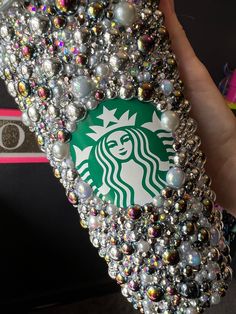 a hand holding a starbucks phone case covered in lots of swaroons and pearls