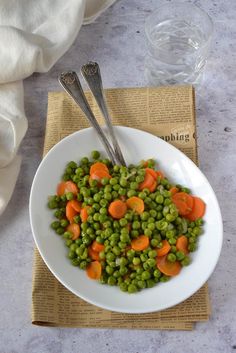 a white bowl filled with peas and carrots on top of a table next to a napkin