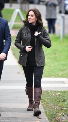 a woman walking down a sidewalk next to a man in a black suit and brown boots