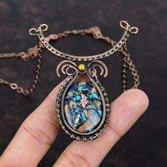 a hand holding a necklace with an image of a woman in blue and gold on it