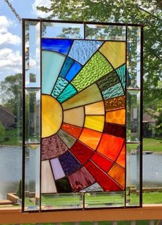 a colorful stained glass window sitting on top of a wooden bench next to a lake