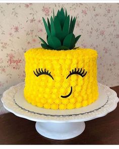 a yellow cake with a pineapple on top and eyes drawn on the side, sitting on a white pedestal