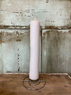 a white candle sitting on top of a wooden table next to a metal holder with a lit candle in it