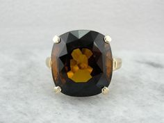 This simple, vintage cocktail mounting with only polished shoulders for decoration, is the perfect canvas for the amazing rich Dravite Tourmaline in the center. The deep, rich brown color is pierced by flickering colors when moved in the light! Dravite Tourmaline is a pleochroic stone, meaning that it reflects more than one color; and this stone dazzles with bright flashes of orange and yellow! Metal: 14K Yellow Gold Gem: Dravite Tourmaline 17.81 Carats Gem Measurements: 16.3 x 14.9 mm, Rectangl Modern Brown Rings For Formal Occasions, Modern Brown Ring For Formal Occasions, Modern Formal Brown Ring, Formal Brown Rings With Polished Finish, Elegant Brown Rings For Formal Occasions, Classic Brown Gemstone Rings, Formal Brown Gemstone Ring, Antique Brown Rings For Formal Occasions, Brown Jewelry With Prong Setting For Formal Occasions