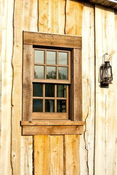 an old window on the side of a wooden building with a lantern hanging from it's side