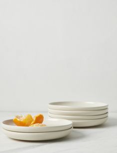 four white plates stacked on top of each other with one orange peel in the middle