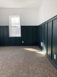 an empty room with dark wood paneling and white window in the corner on the far wall