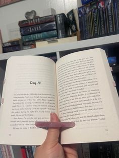 a person holding an open book in front of a bookshelf full of books