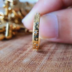 a close up of a person's hand holding a gold ring with flowers on it