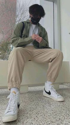 a man sitting on top of a window sill while looking at his cell phone