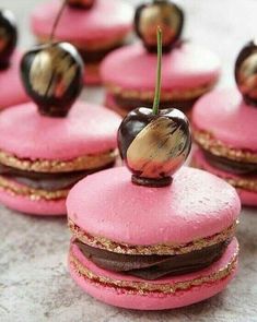 several pink macaroons with chocolate covered cherries on top and one cherry in the middle