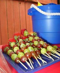 grapes and strawberries are arranged on skewers in front of a blue pail