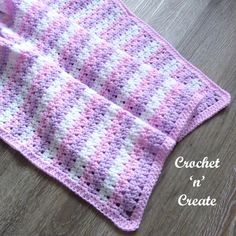 a pink and white crocheted blanket laying on top of a wooden floor next to a cup