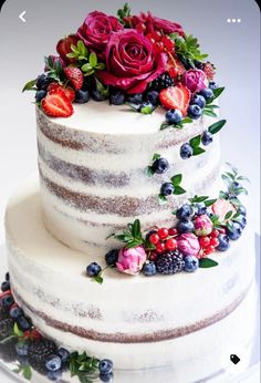 a three layer cake decorated with fresh berries and flowers