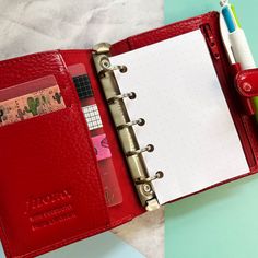 an open red leather planner book next to a pen