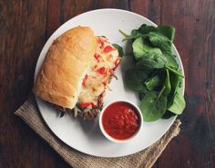 a white plate topped with a sandwich next to a bowl of ketchup and spinach