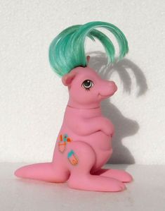 a pink toy with green hair sitting on top of a white table next to a wall