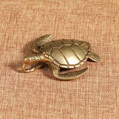 a turtle brooch sitting on top of a brown cloth next to a white and black cat