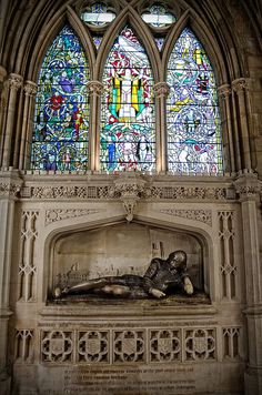 a large stained glass window above a statue in a church with an elaborate stone fireplace