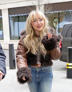 a blonde woman walking down the street with her hand in her pockets and holding onto a teddy bear